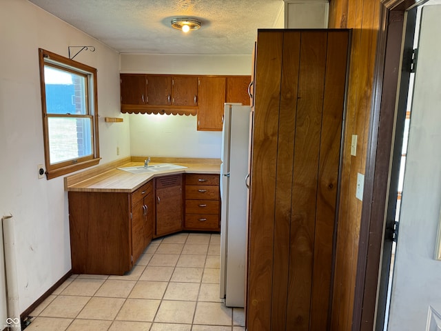 kitchen featuring a textured ceiling, white fridge, sink, and light tile patterned floors