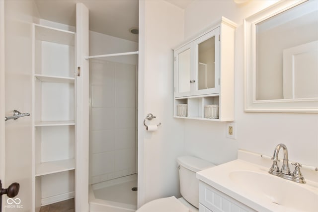 bathroom with toilet, a tile shower, and vanity