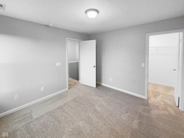 unfurnished bedroom with light colored carpet, a walk in closet, and a closet