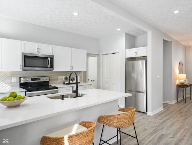 kitchen with appliances with stainless steel finishes, sink, a textured ceiling, white cabinets, and a breakfast bar