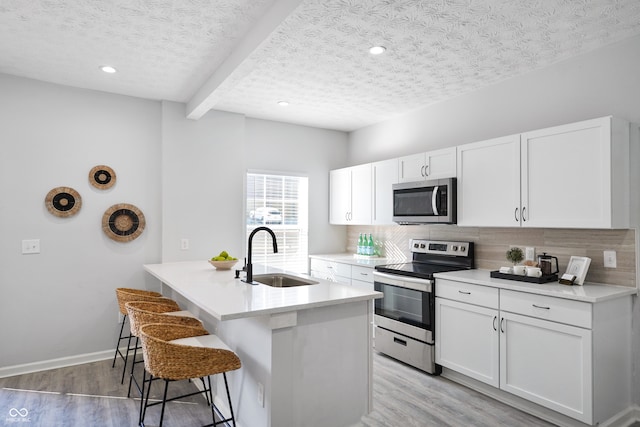 kitchen featuring appliances with stainless steel finishes, white cabinetry, a kitchen island with sink, and sink