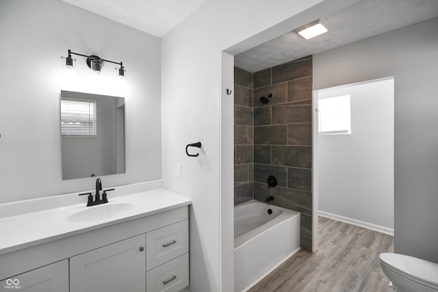 full bathroom featuring a textured ceiling, hardwood / wood-style floors, toilet, tiled shower / bath, and vanity