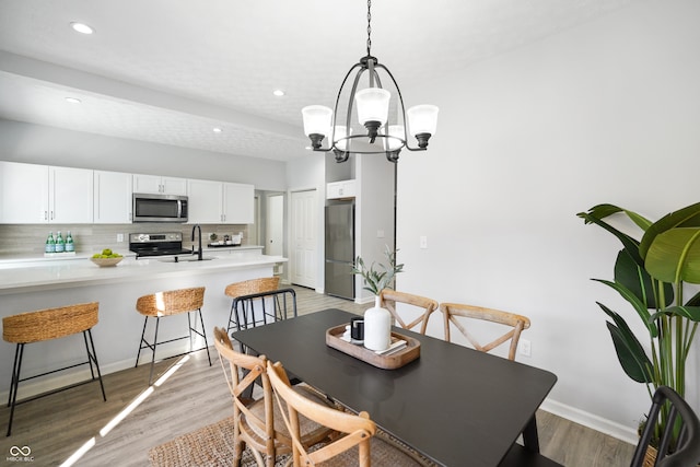 dining area with an inviting chandelier, sink, and light wood-type flooring