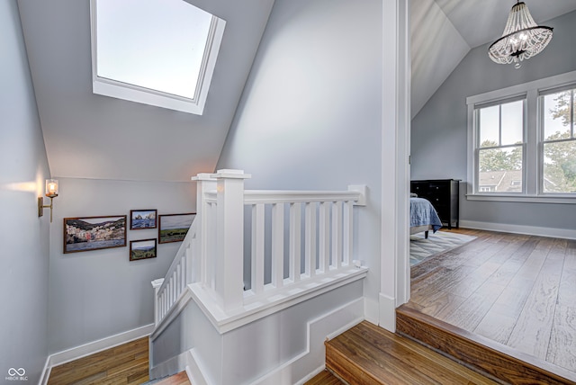 staircase with hardwood / wood-style flooring, vaulted ceiling with skylight, and a notable chandelier