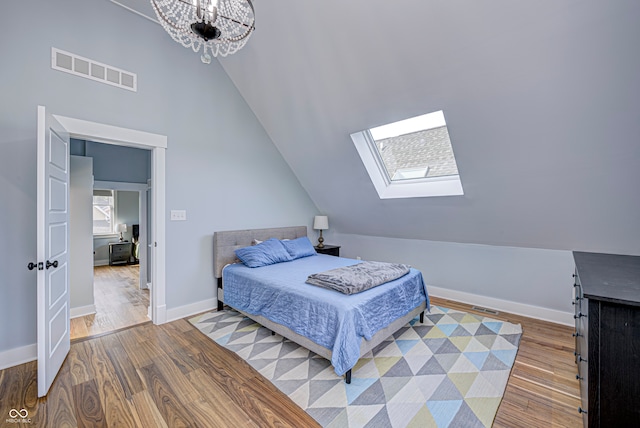 bedroom with wood-type flooring, lofted ceiling with skylight, and a chandelier