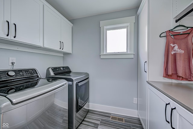 clothes washing area with cabinets and washing machine and clothes dryer