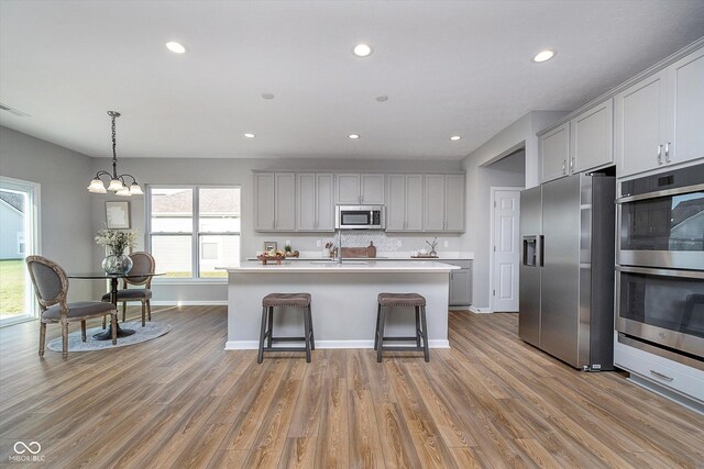 kitchen featuring light hardwood / wood-style flooring, appliances with stainless steel finishes, gray cabinets, a kitchen breakfast bar, and a kitchen island with sink