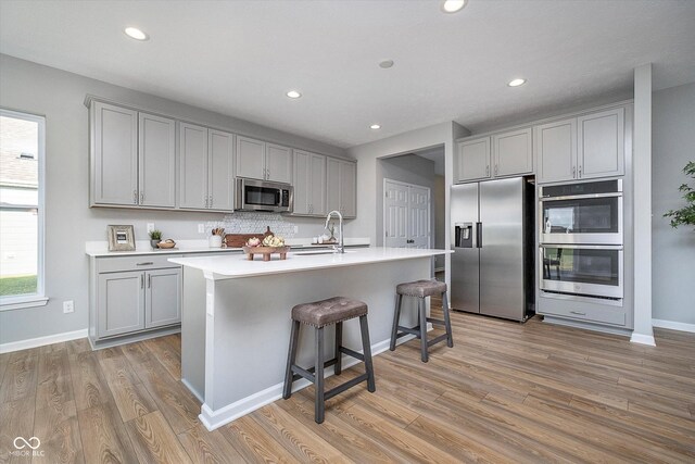 kitchen with a center island with sink, light wood-type flooring, gray cabinets, and appliances with stainless steel finishes