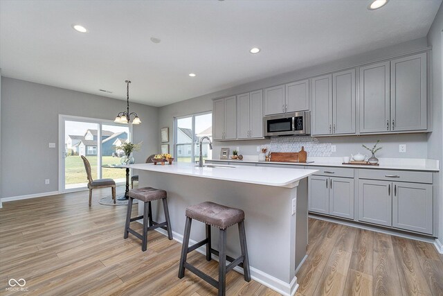 kitchen with gray cabinetry, sink, light wood-type flooring, and a notable chandelier