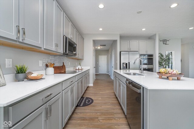 kitchen with gray cabinets, stainless steel appliances, a kitchen island with sink, and light wood-type flooring