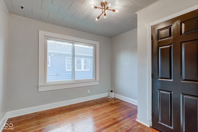 spare room featuring a chandelier, a healthy amount of sunlight, crown molding, and light hardwood / wood-style flooring