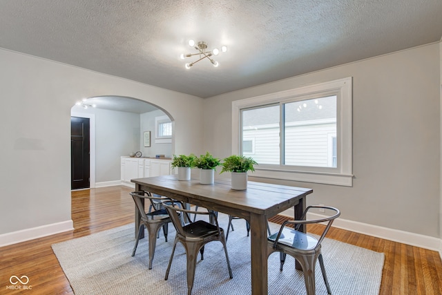 dining space featuring hardwood / wood-style flooring, a notable chandelier, and a textured ceiling