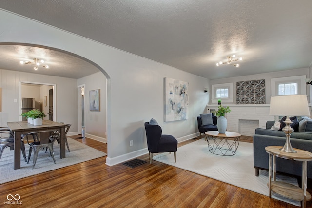 living room featuring hardwood / wood-style flooring, a fireplace, a textured ceiling, and an inviting chandelier