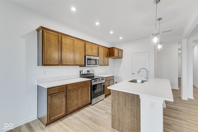 kitchen featuring a kitchen island with sink, hanging light fixtures, sink, appliances with stainless steel finishes, and light hardwood / wood-style floors