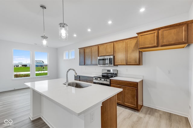 kitchen with an island with sink, stainless steel appliances, hanging light fixtures, and sink