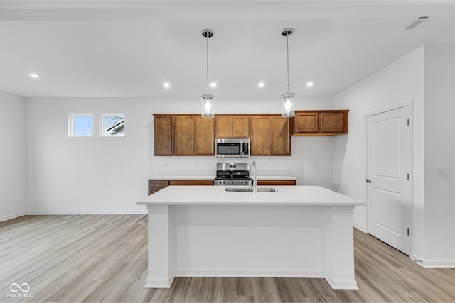 kitchen featuring sink, light hardwood / wood-style flooring, an island with sink, decorative light fixtures, and stainless steel appliances