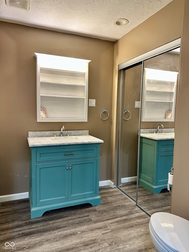 bathroom with wood-type flooring, vanity, a textured ceiling, and toilet