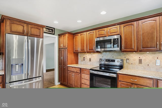 kitchen featuring light wood-type flooring, light stone counters, stainless steel appliances, and tasteful backsplash