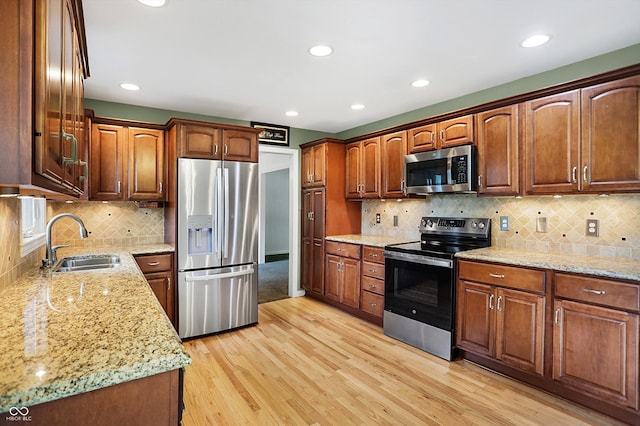 kitchen featuring tasteful backsplash, stainless steel appliances, sink, light stone countertops, and light hardwood / wood-style floors