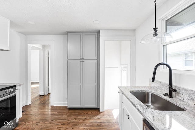 kitchen featuring dark wood-type flooring, sink, light stone countertops, decorative light fixtures, and gray cabinets