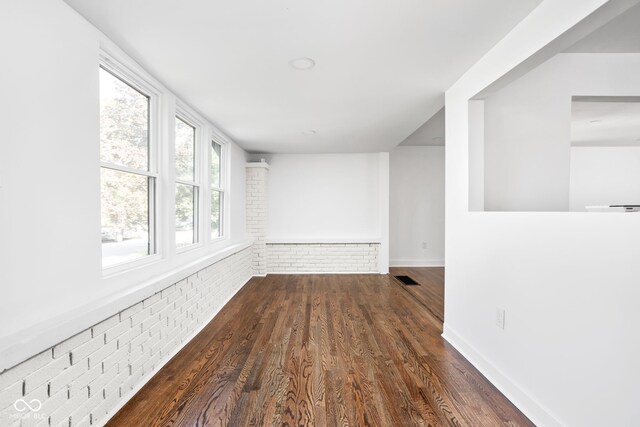 unfurnished room featuring brick wall and dark wood-type flooring