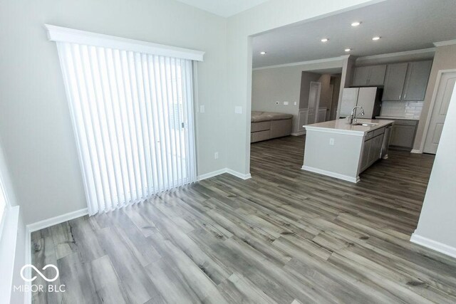 kitchen with gray cabinetry, light hardwood / wood-style floors, a kitchen island with sink, crown molding, and sink