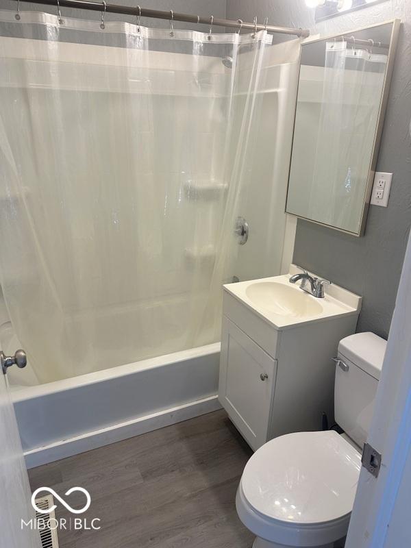 full bathroom featuring hardwood / wood-style floors, toilet, shower / tub combo with curtain, and vanity