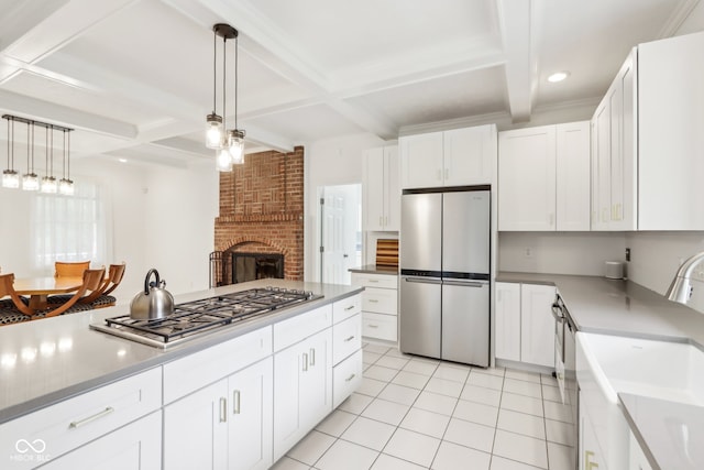 kitchen featuring appliances with stainless steel finishes, hanging light fixtures, a brick fireplace, white cabinets, and beamed ceiling