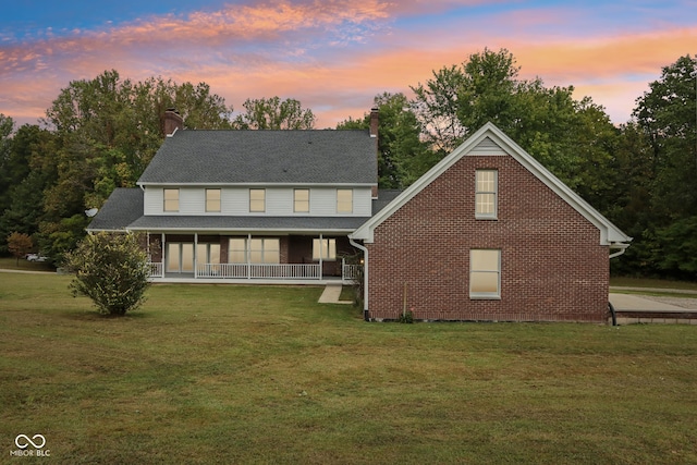 back house at dusk featuring a yard and covered porch