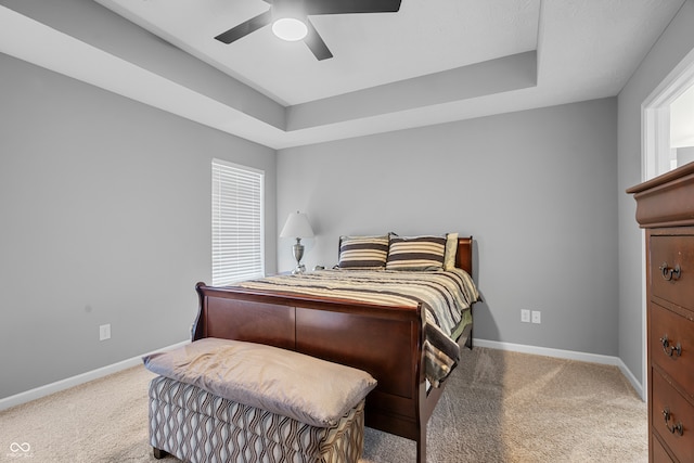 carpeted bedroom with ceiling fan and a raised ceiling