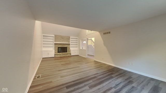 unfurnished living room with built in features, a fireplace, and hardwood / wood-style floors