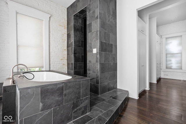 bathroom with wood-type flooring, brick wall, and a tub