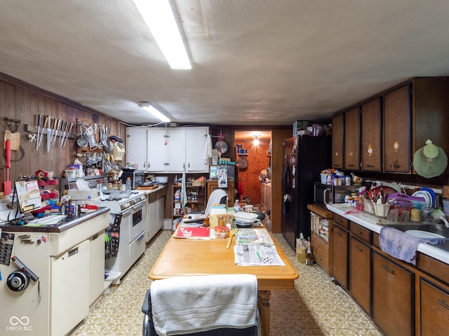 kitchen featuring stainless steel stove, white cabinets, wooden walls, and black refrigerator