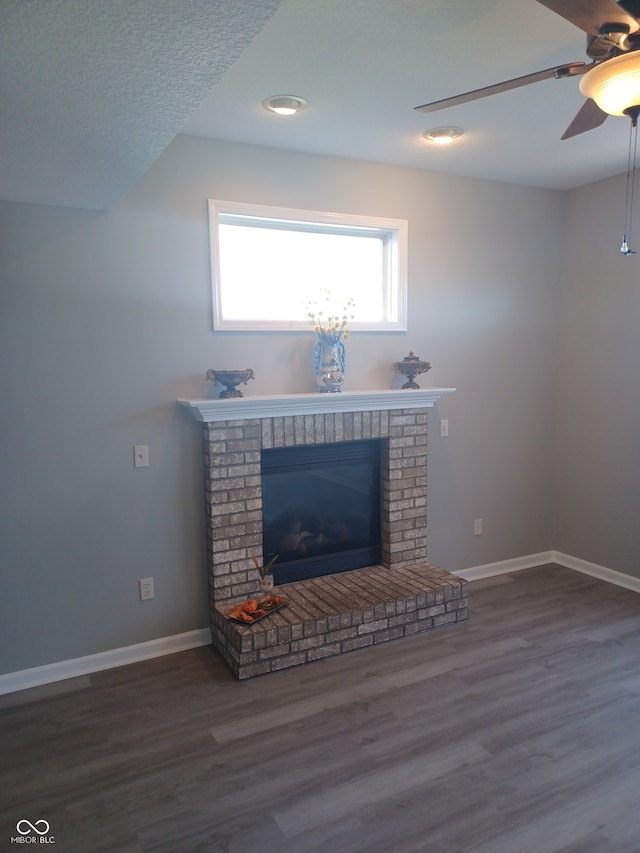 unfurnished living room with hardwood / wood-style floors, ceiling fan, a textured ceiling, and a brick fireplace