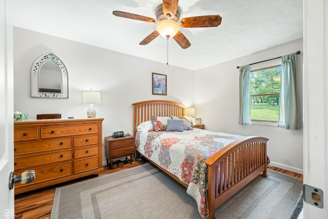 bedroom featuring ceiling fan, hardwood / wood-style floors, and a textured ceiling