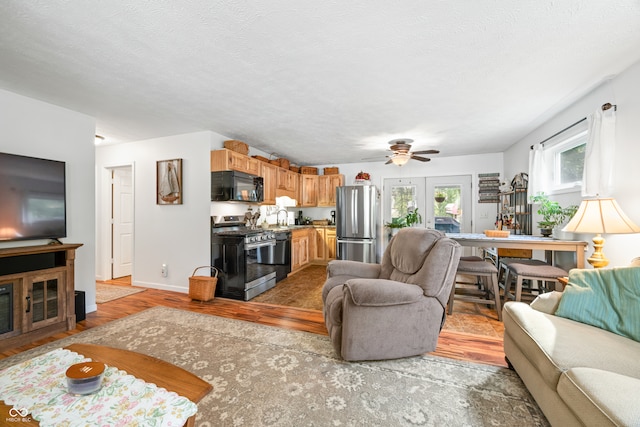 living room featuring a textured ceiling, ceiling fan, and light hardwood / wood-style flooring