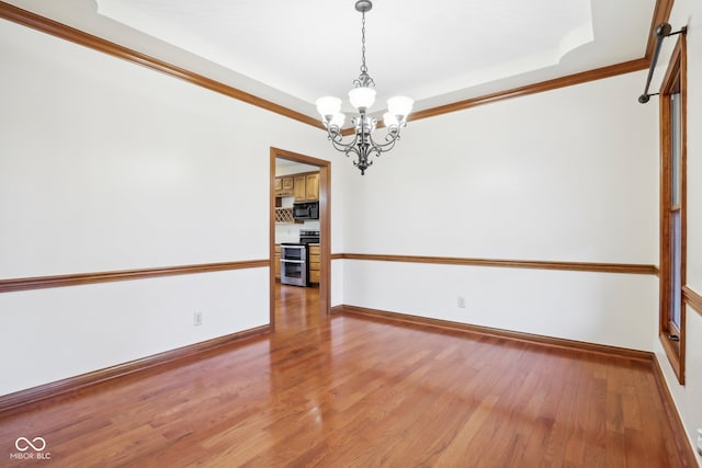 spare room with a chandelier, wood-type flooring, a raised ceiling, and ornamental molding