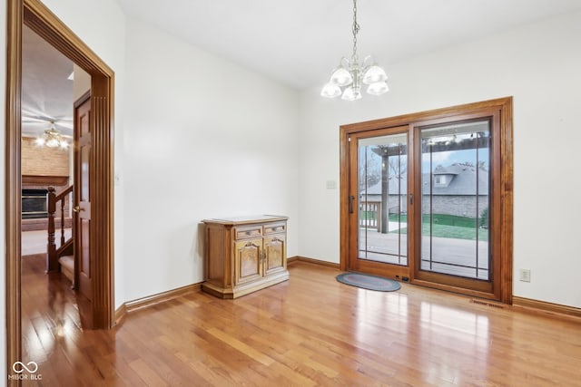 doorway with a brick fireplace, ceiling fan with notable chandelier, and light hardwood / wood-style flooring