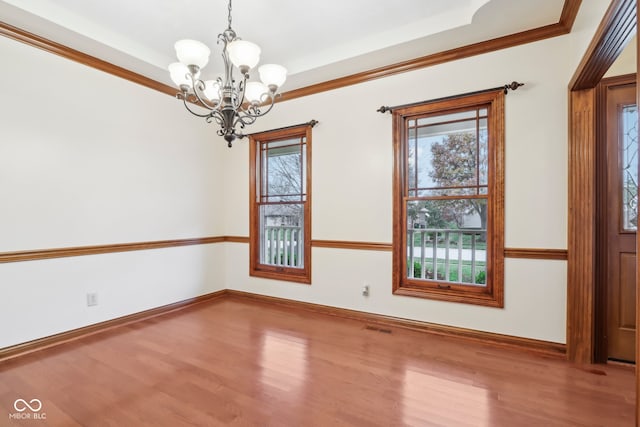 spare room with hardwood / wood-style flooring, a raised ceiling, ornamental molding, and an inviting chandelier