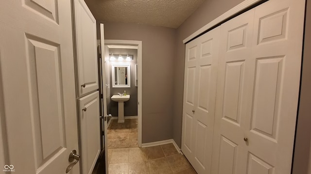 hall featuring light tile patterned flooring, a textured ceiling, and sink