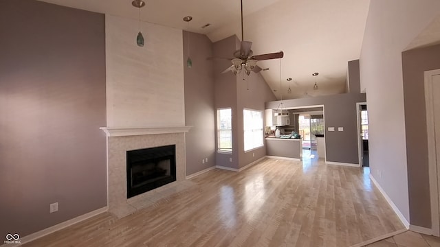 unfurnished living room featuring high vaulted ceiling, a tiled fireplace, ceiling fan, and light hardwood / wood-style flooring