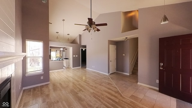 unfurnished living room with high vaulted ceiling, a tiled fireplace, ceiling fan, and light hardwood / wood-style floors