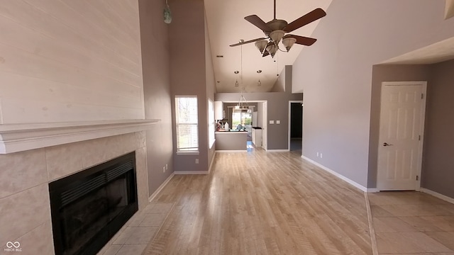 unfurnished living room with high vaulted ceiling, a fireplace, ceiling fan, and light wood-type flooring