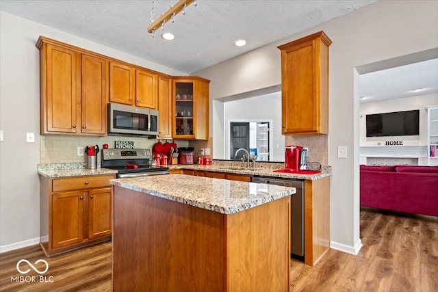 kitchen featuring a textured ceiling, sink, stainless steel appliances, hardwood / wood-style floors, and light stone countertops