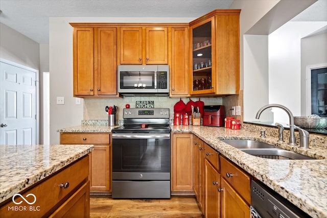 kitchen featuring light wood-type flooring, sink, backsplash, appliances with stainless steel finishes, and light stone countertops