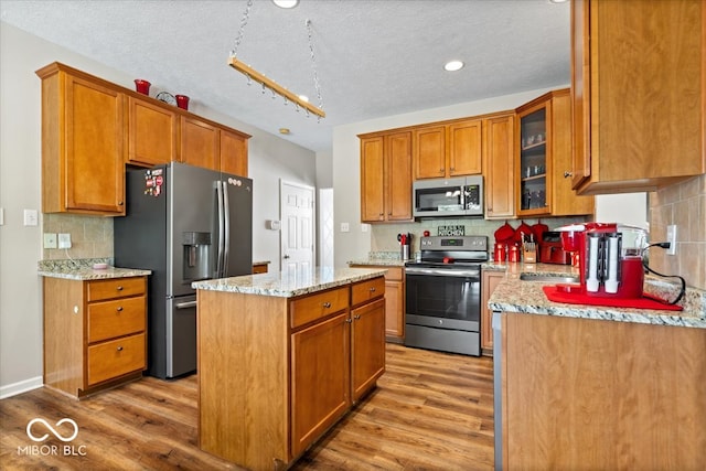 kitchen with a textured ceiling, appliances with stainless steel finishes, a center island, light stone countertops, and light hardwood / wood-style floors