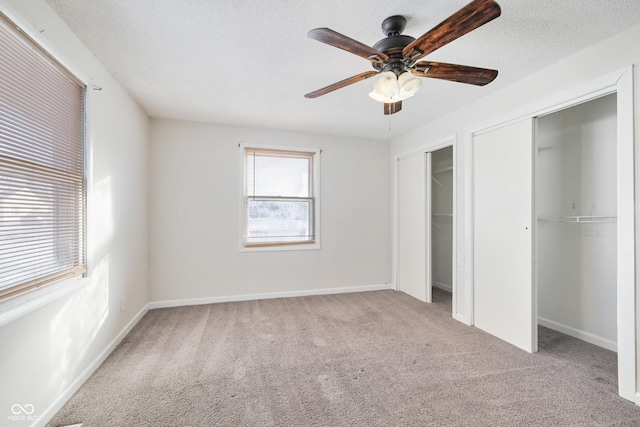 unfurnished bedroom with two closets, light carpet, a textured ceiling, and ceiling fan