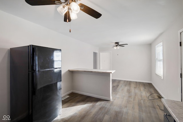 kitchen with dark wood-type flooring, kitchen peninsula, ceiling fan, and black fridge