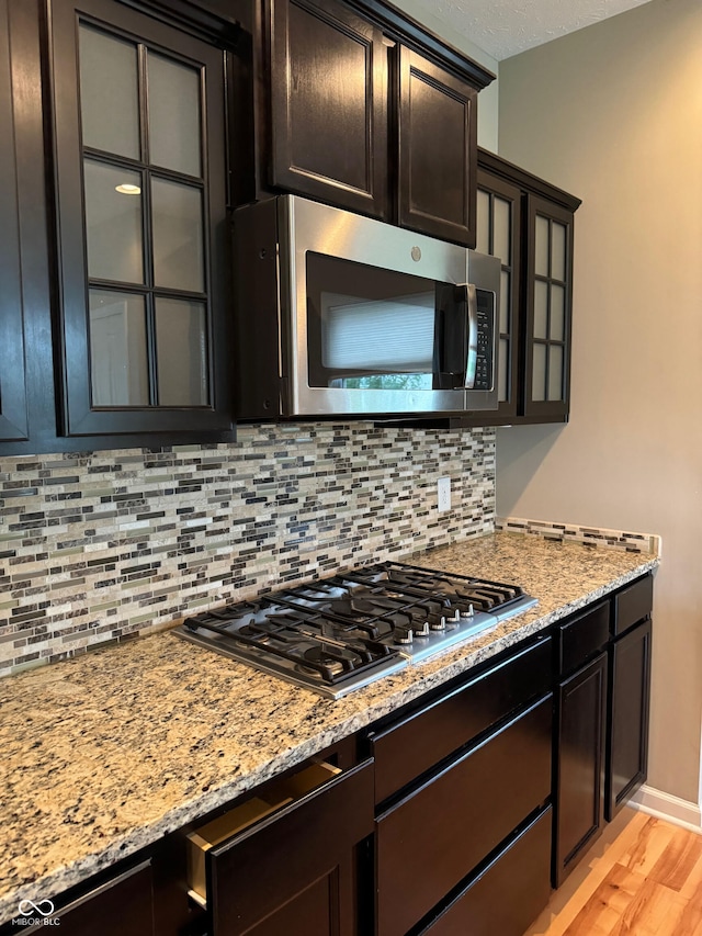 kitchen featuring light stone countertops, light hardwood / wood-style flooring, stainless steel appliances, and tasteful backsplash