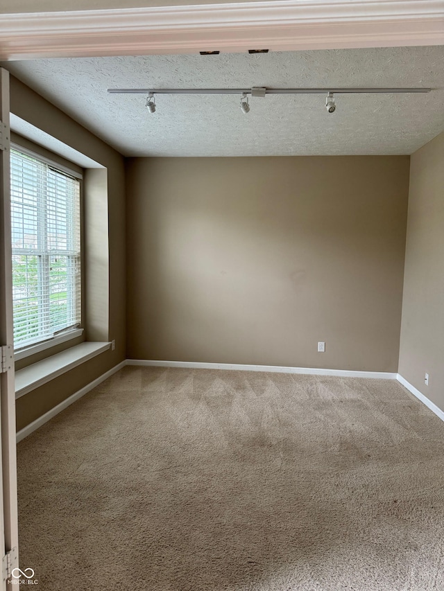 empty room with a textured ceiling, carpet flooring, and rail lighting